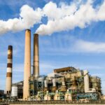 A large industrial power plant with smokestacks emitting smoke under a blue sky, symbolizing pollution.